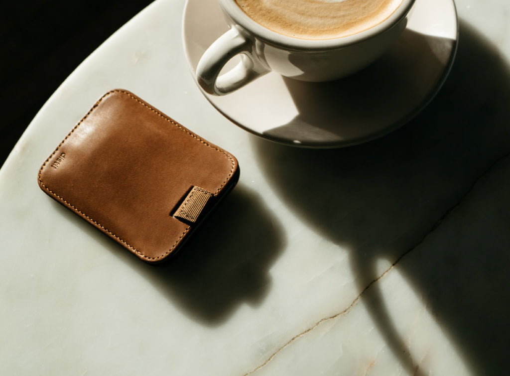 A well-worn brown leather wallet sits on a marble table beside a cup of coffee
